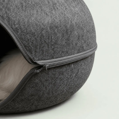 Gros plan sur la fermeture éclair du lit-tunnel donut en feutre gris, chat blanc lové à l'intérieur