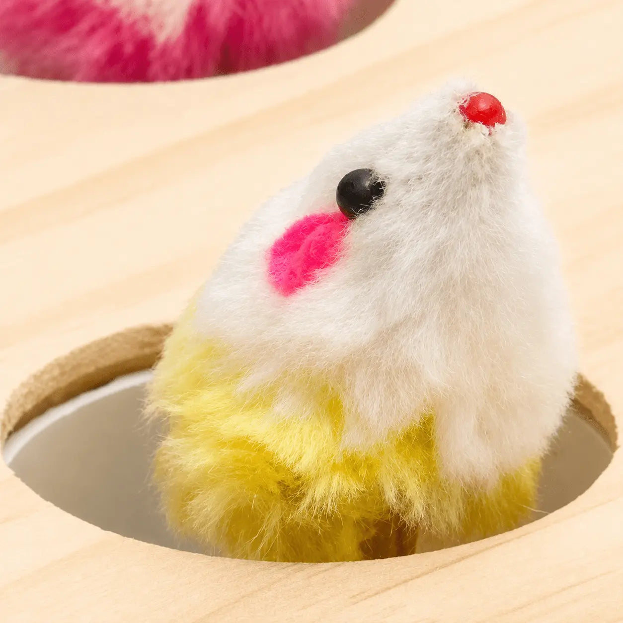 Gros plan sur une souris en peluche colorée surgissant d'un trou du jouet interactif en bois